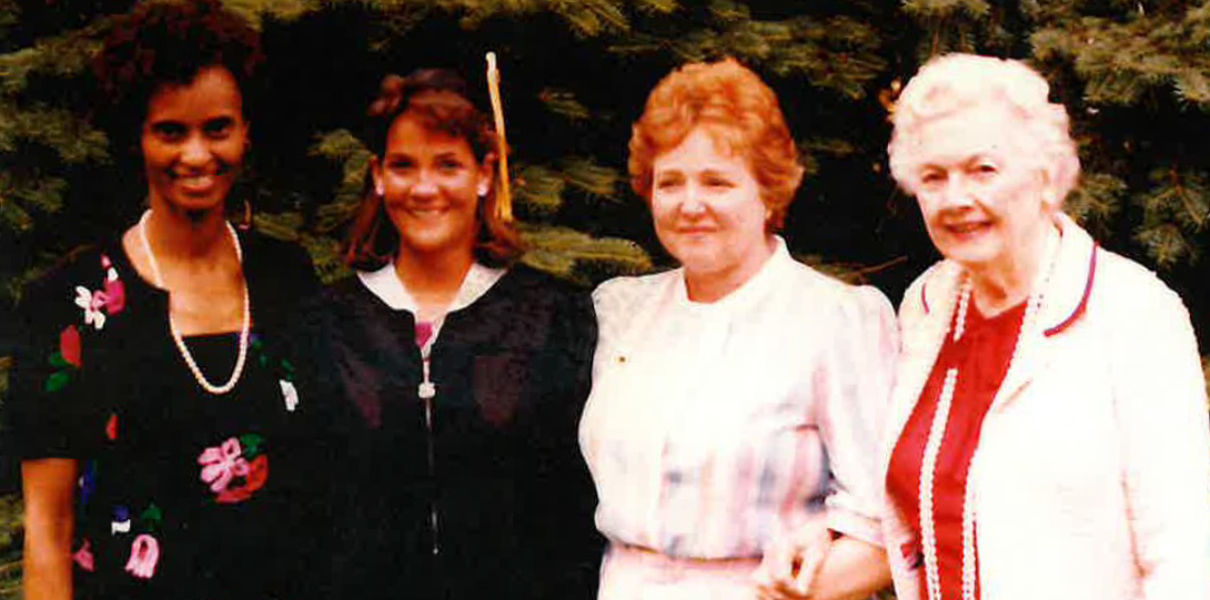 A group of 4 women standing in front of trees smiling.