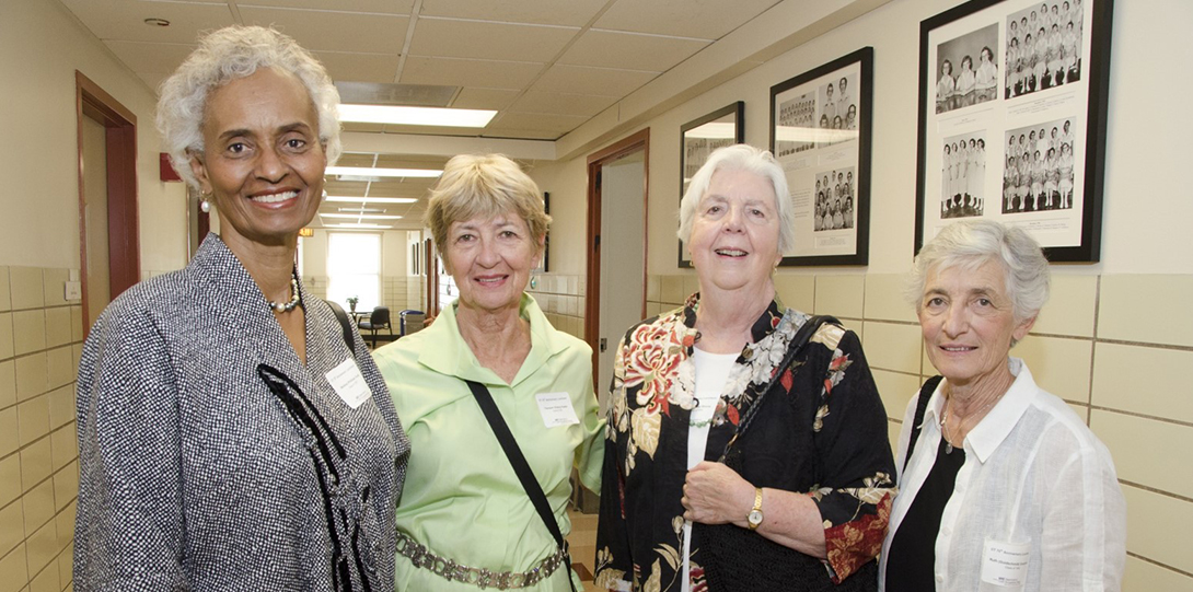 Four women in the middle of a hallway smiling at the camera.