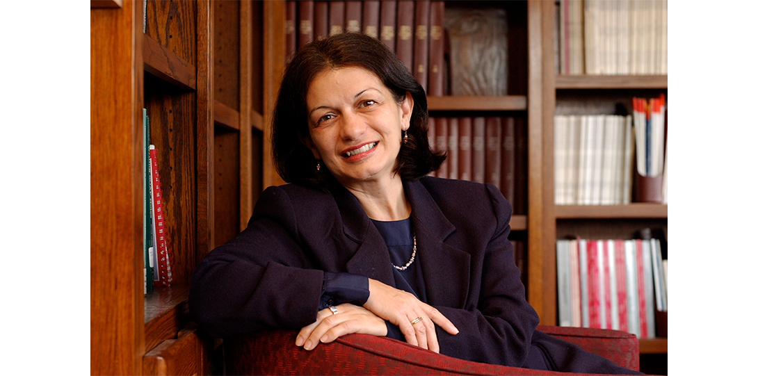 A woman seated in front of a bookcase, smiling at the camera.