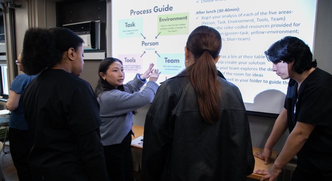 A group of students gather around a projection screen in a classroom