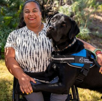 Woman in wheelchair next to a large, black service dog. 